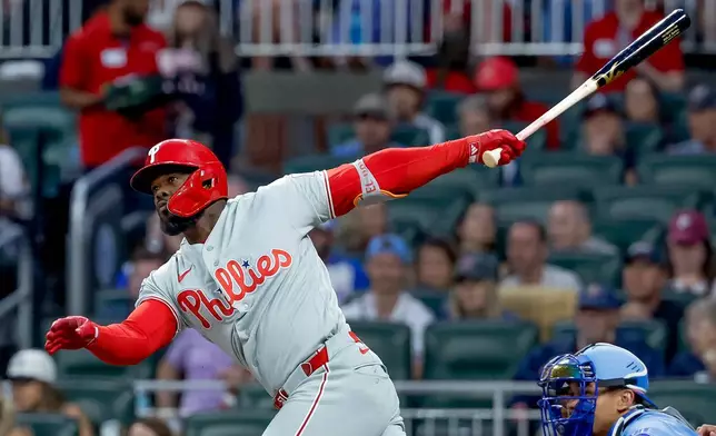 Philadelphia Phillies' Adolis Garcia, left, hits an RBI triple as Atlanta Braves catcher Drake Baldwin, right, looks on during the first inning of a baseball game, Saturday, April 25, 2026, in Atlanta. (AP Photo/Erik S. Lesser)