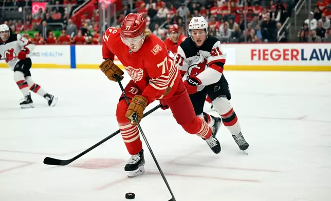 Detroit Red Wings defenseman Simon Edvinsson (77) moves the puck away from New Jersey Devils center Dawson Mercer, back right, during the first period of an NHL hockey game, Saturday, April 11, 2026, in Detroit. (AP Photo/Jose Juarez)