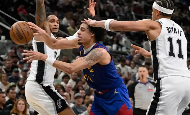 Denver Nuggets guard Julian Strawther, center, tangles with San Antonio Spurs players Carter Bryant (11) and Devin Vassell during the second half of an NBA basketball game, Sunday, April 12, 2026, in San Antonio. (AP Photo/Darren Abate)