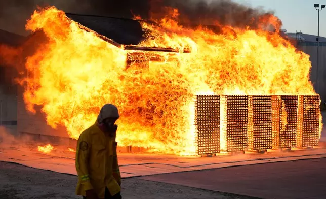 A wildfire researcher walks in front of an accessory dwelling unit burning during an experiment at the Institute for Business &amp; Home Safety center on Thursday, April 16, 2026, in Richburg, S.C. (AP Photo/Erik Verduzco)