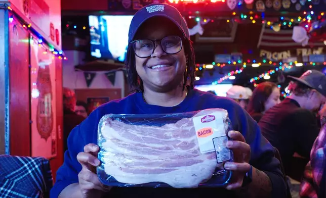 In this image made from video, Ashley Burris holds up a pack of bacon she won during a meat raffle at the 1029 Bar in Minneapolis, April 3, 2026. (AP Photo/Mark Vancleave)