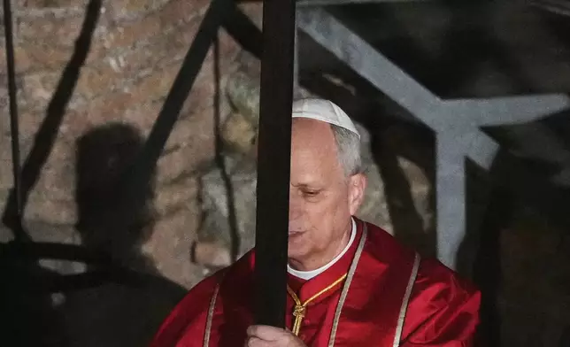 Pope Leo XIV carries a lightweight, 1.5-meter (5-foot) wooden cross during the Via Crucis, the torchlit Good Friday Stations of the Cross procession at the Colosseum in Rome, Friday, April 3, 2026, which symbolically retraces Jesus Christ's steps to his crucifixion on Calvary in Jerusalem. (AP Photo/Alessandra Tarantino)
