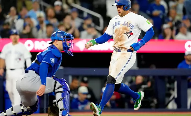 Toronto Blue Jays' George Springer, right, scores on a single against the Los Angeles Dodgers during first-inning baseball game action in Toronto, Monday, April 6, 2026. (Frank Gunn/The Canadian Press via AP)