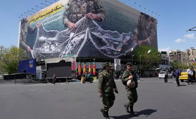 FILE - Two police officers walk in front of an anti-U.S. billboard depicting American aircraft being caught by Iranian armed forces in a fishing net beneath the words in Farsi, "The Strait of Hormuz will remain closed, The entire Persian Gulf is our hunting ground," in Tehran, Iran, Sunday, April 5, 2026. (AP Photo/Vahid Salemi, File)