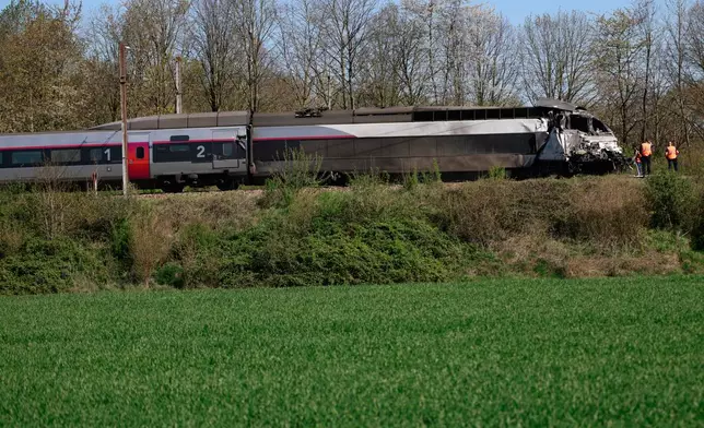 Railway workers stand near a high-speed train (TGV) after it crashed into a truck carrying military equipment in Bully-les-Mines, northern France, Tuesday, April 7, 2026. (AP Photo/Jean-Francois Badias)