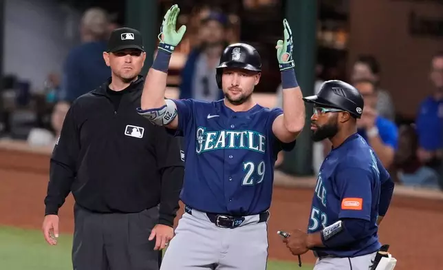 Seattle Mariners' Cal Raleigh (29) celebrates hitting a run-scoring single as first base coach Eric Young Jr., right, and umpire Brock Ballou, left, look on in the fifth inning of a baseball game against the Texas Rangers Tuesday, April 7, 2026, in Arlington, Texas. (AP Photo/Tony Gutierrez)