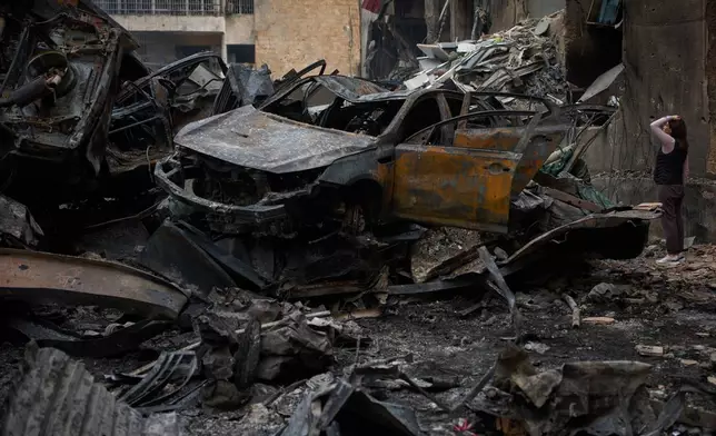 A resident checks damage to buildings as she walks near charred cars, at the site of Wednesday's Israeli airstrike, in Beirut, Lebanon, Friday, April 10, 2026. (AP Photo/Emilio Morenatti)