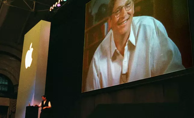 FILE - Apple Computer Inc. co-founder and current adviser Steve Jobs, background left, stands at a podium as Bill Gates, chief executive of Microsoft Corp., appears on a video screen as he addresses the MacWorld convention praising the new alliance between Apple and Microsoft Wednesday, Aug. 6, 1997, in Boston. (AP Photo/Julia Malakie, File)