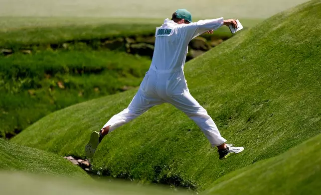 Gary Woodland's caddie Brennan Little leaps cross Rea's Creek on the 13th hole during the second round of the Masters golf tournament at the Augusta National Golf Club, Friday, April 10, 2026, in Augusta, Ga. (AP Photo/Matt Slocum)