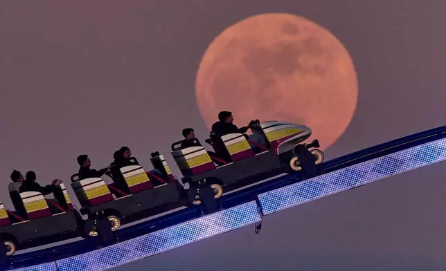 People ride a roller coaster past the full moon on the funfair in Frankfurt, Germany, Wednesday, April 1, 2026. (AP Photo/Michael Probst)
