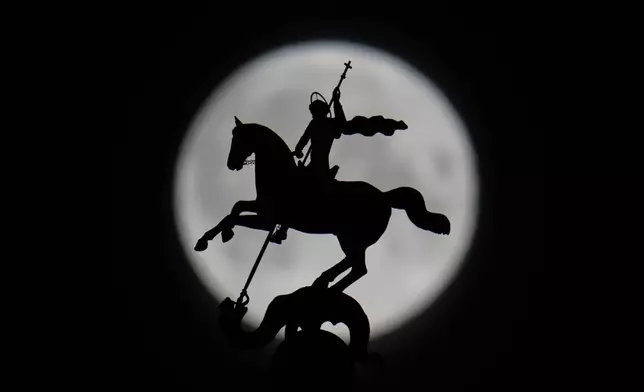 The full moon rises behind the statue of St. George atop of a bilding in Moscow, early Thursday, April 2, 2026. (AP Photo/Pavel Bednyakov)