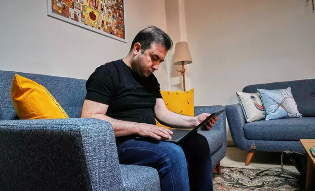 Mehdi Alishir looks at his laptop in his living room in Tehran, Iran, Sunday, April 5, 2026. (AP Photo/Vahid Salemi)