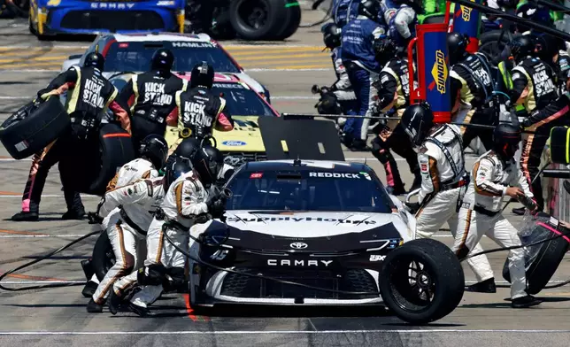 Tyler Reddick, front, and make stop on pit road for a tire change after the first stage during a NASCAR Cup Series auto race at Kansas Speedway in Kansas City, Kan., Sunday, April 19, 2026. (AP Photo/Colin E. Braley)
