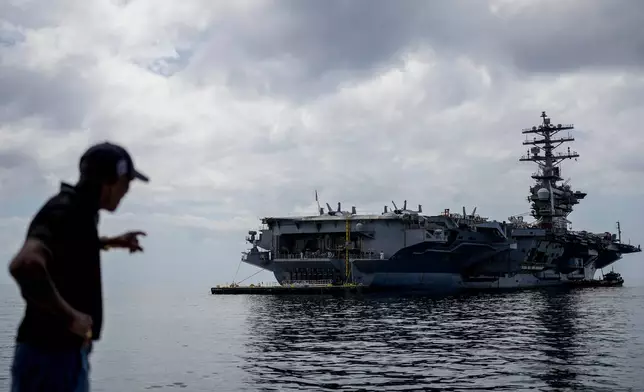 FILE - A worker points to the U.S. Navy aircraft carrier USS Nimitz docking in the Gulf of Panama, March 30, 2026. (AP Photo/Matias Delacroix, File)