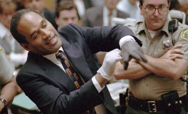 FILE - In this June 15, 1995 file photo, O.J. Simpson, left, grimaces as he tries on one of the leather gloves prosecutors say he wore the night his ex-wife Nicole Brown Simpson and Ron Goldman were murdered in a Los Angeles courtroom. (AP Photo/Sam Mircovich, Pool, file)