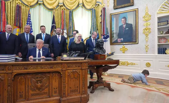 Travis Smith, 2, crawls on the floor as President Donald Trump speaks during an event on health care affordability in the Oval Office at the White House, Thursday, April 23, 2026, in Washington. (AP Photo/Mark Schiefelbein)