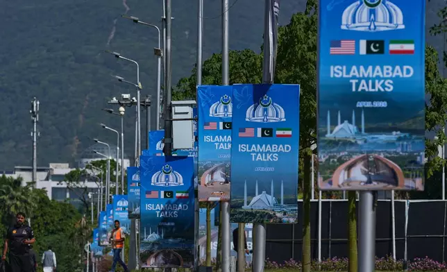 Workers walk past billboards near the Serena Hotel ahead of the second round of negotiations between the U.S. and Iran, in Islamabad, Pakistan, Monday, April 20, 2026. (AP Photo/Anjum Naveed)