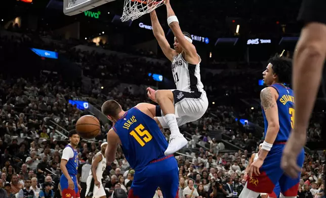 San Antonio Spurs forward Carter Bryant (11) dunks over Denver Nuggets center Nikola Jokic during the first half of an NBA basketball game, Sunday, April 12, 2026, in San Antonio. (AP Photo/Darren Abate)