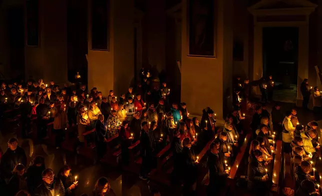 Worshippers hold candles during the Easter vigil Mass in the Cathedral Basilica of Vilnius, Lithuania, late Saturday, April 4, 2026. (AP Photo/Mindaugas Kulbis)