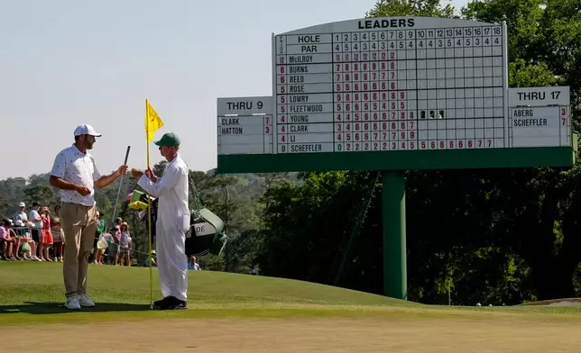Scottie Scheffler gives his club to his caddie on the 18th hole during the third round of the Masters golf tournament at the Augusta National Golf Club, Saturday, April 11, 2026, in Augusta, Ga. (AP Photo/David J. Phillip)
