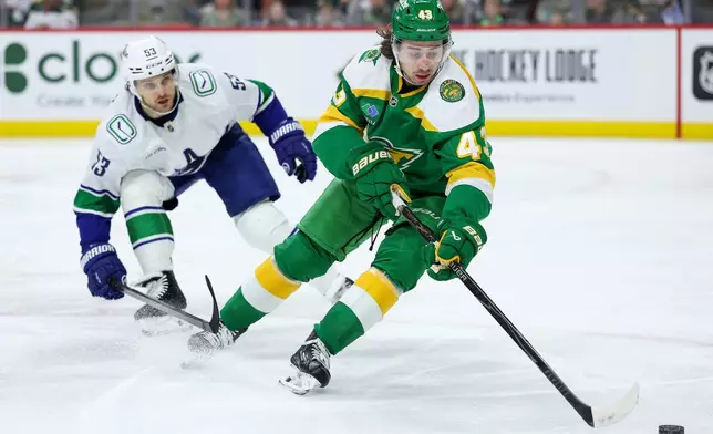 Minnesota Wild defenseman Quinn Hughes, right, skates with the puck as Vancouver Canucks center Teddy Blueger (53) defends during the second period of an NHL hockey game Thursday, April 2, 2026, in St. Paul, Minn. (AP Photo/Matt Krohn)