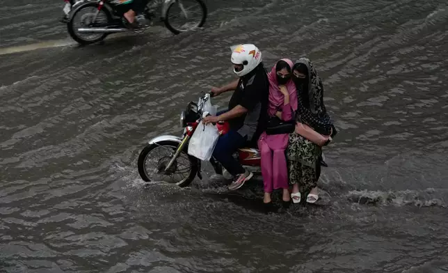 Women ride on the back of a motorcycle over floodwaters after heavy rain in Lahore, Pakistan, Tuesday, April 7, 2026. (AP Photo/K.M. Chaudary)