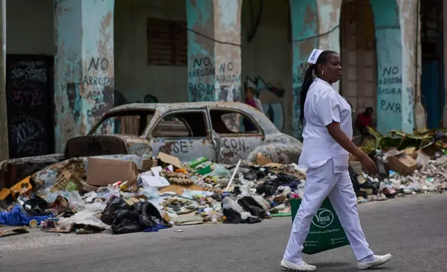 A nurse walks past trash and an abandoned classic American car on a street in Havana, Wednesday, April 22, 2026. (AP Photo/Ramon Espinosa)