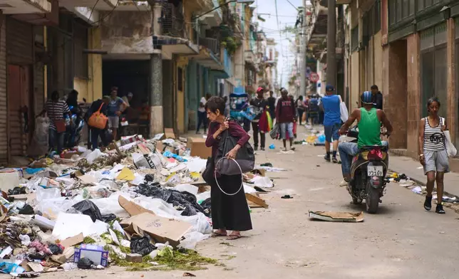 A pedestrian looks for items to salvage in a pile of trash on a street in Havana, Wednesday, April 22, 2026. (AP Photo/Ramon Espinosa)