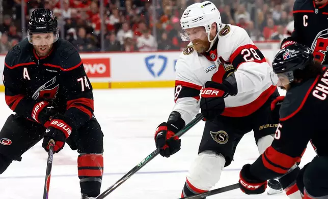 Ottawa Senators' Claude Giroux (28) battles for the puck with Carolina Hurricanes' Jalen Chatfield, right, and Jaccob Slavin (74) during the first period of Game 2 of an NHL hockey Stanley Cup first-round playoff series in Raleigh, N.C., Monday, April 20, 2026. (AP Photo/Karl DeBlaker)