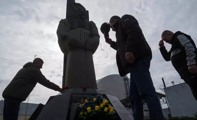 Workers who helped clean up contamination from the Chernobyl nuclear power plant accident place flowers at a monument at the facility in Chernobyl, Ukraine, Tuesday, April 21, 2026. (AP Photo/Evgeniy Maloletka)
