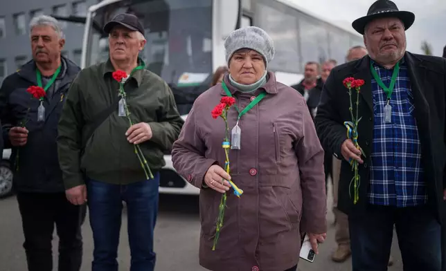 Workers who helped clean up contamination from the Chernobyl nuclear power plant disaster hold flowers before placing them on a monument to their fallen comrades near the plant in Chernobyl, Ukraine, Tuesday, April 21, 2026. (AP Photo/Evgeniy Maloletka)