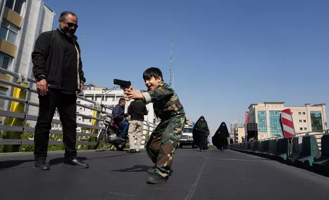 A boy plays with a toy gun on the sidelines of a state-organized rally supporting the supreme leader, marking National Girls' Day, in Tehran, Iran, Friday, April 17, 2026. (AP Photo/Vahid Salemi)