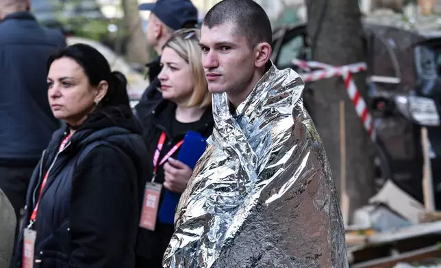 A man covered in thermal blanket stands in a yard of a residential building damaged by a Russian strike on Dnipro, Ukraine, Saturday, April 25, 2026. (AP Photo/Mykola Synelnykov)