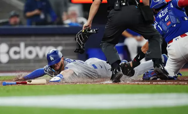 Los Angeles Dodgers' Alex Freeland, left, slides in safely at home ahead of the tag from Toronto Blue Jays catcher Brandon Valenzuela (59) during the ninth inning of an MLB baseball game in Toronto on Tuesday, April 7, 2026. (Nathan Denette/The Canadian Press via AP)