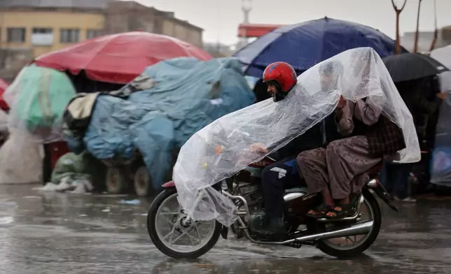 A man rides a motorcycle with two passengers under a plastic cover through heavy rain in Kabul, Afghanistan, Tuesday, March 31, 2026. (AP Photo/Siddiqullah Alizai)