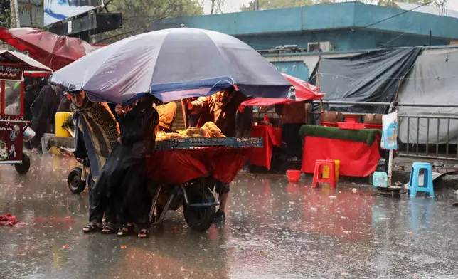 Residents take cover from heavy rain under the umbrella of a food stall at a market in Kabul, Afghanistan, Tuesday, March 31, 2026. (AP Photo/Siddiqullah Alizai)