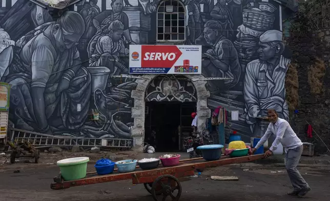 A fisherman pushes his cart filled with catch as he passes by a mural of the fisher community at Sassoon Dock In Mumbai, India, Wednesday, April 8, 2026. (AP Photo/Rafiq Maqbool)