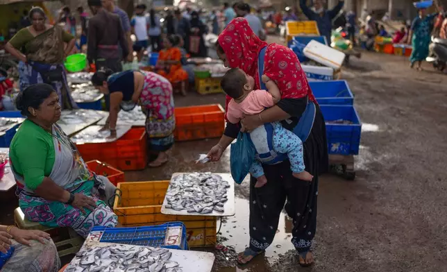 A woman carrying her child checks out fresh fish at at Bhaucha Dhaka in Mumbai, India, Wednesday, April 8, 2026. (AP Photo/Rafiq Maqbool)