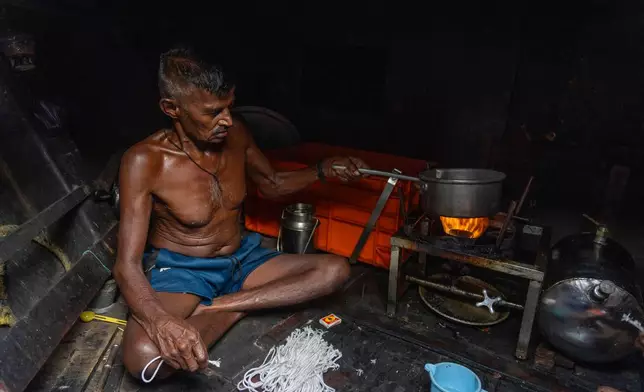 A fisherman prepares tea on a stove in a boat anchored due the price high at Sassoon Dock in Mumbai, India, Tuesday, April 7, 2026. (AP Photo/Rafiq Maqbool)