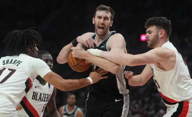 San Antonio Spurs center Luke Kornet, center, and Portland Trail Blazers center Donovan Clingan, right, battle for control of the ball during the second half in Game 3 of a first-round NBA playoffs basketball series in Portland, Ore, Friday, April 24, 2026. (AP Photo/Jenny Kane)