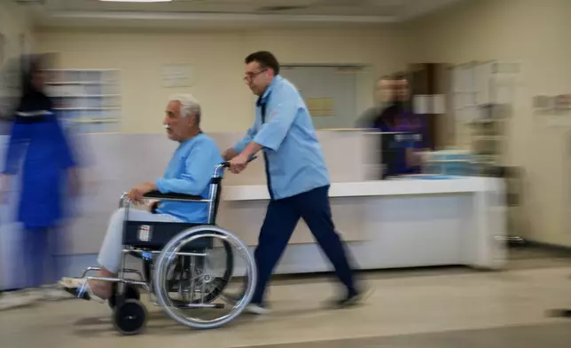 A patient in a wheelchair is pushed along a corridor at Shohadaye Tajrish Hospital in Tehran, Iran, Tuesday, April 7, 2026. (AP Photo/Francisco Seco)