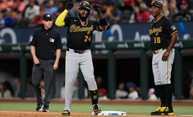 Pittsburgh Pirates' Marcell Ozuna (24) celebrates a run-scoring single as first base coach Tarrik Brock (16) and umpire Dan Merzel, left, look on in the first inning of a baseball game against the Texas Rangers Wednesday, April 22, 2026, in Arlington, Texas. (AP Photo/Tony Gutierrez)