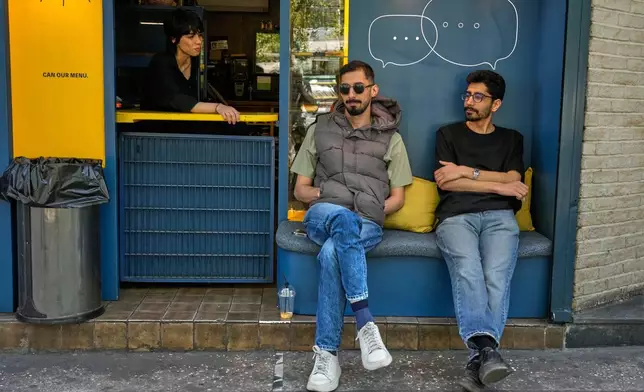 A cafe attendant sits at the counter as two men sit at a cafe in downtown Tehran, Iran, Sunday, April 5, 2026. (AP Photo/Vahid Salemi)
