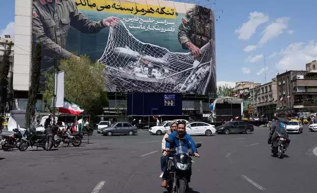 Vehicles and motorcycles move past an anti-U.S. billboard depicting the American aircrafts into the Iranian armed forces fishing net with signs that read in Farsi: "The Strait of Hormuz will remain closed, The entire Persian Gulf is our hunting ground," at the Eqelab-e-Eslami, or Islamic Revolution square in downtown Tehran, Iran, Sunday, April 5, 2026. (AP Photo/Vahid Salemi)