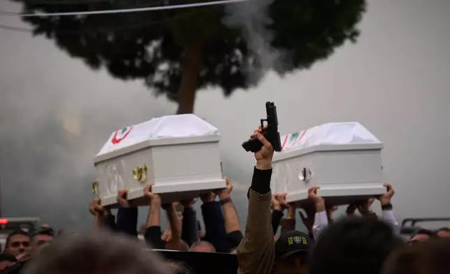 A gunman fires his gun as men carry the coffins with the bodies of Pierre Mouawad, an official with the anti-Hezbollah Lebanese Forces party, and his wife during their funeral in Yahshush, in Lebanon, Tuesday, April 7, 2026. (AP Photo/Emilio Morenatti)