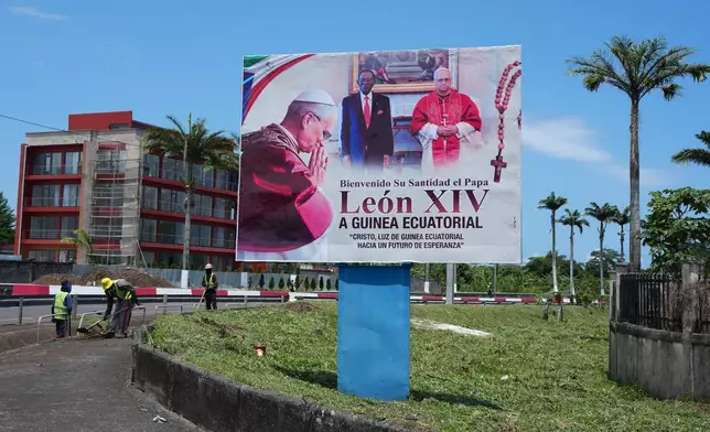 People work near a billboard featuring Pope Leo XIV, right, and Equatorial Guinea's President Teodoro Obiang Nguema Mbasogo, ahead of the Pope's visit in Malabo, Equatorial Guinea, Friday, April 17, 2026. (AP Photo/Misper Apawu)