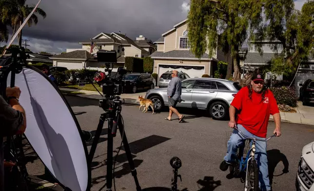 Pedestrians walk past the home, middle back, connected to Cole Tomas Allen, who was identified as the suspect at the White House Correspondents Dinner shooting, as members of the media stage, in Torrance, Calif., Sunday, April 26, 2026. (Stephen Lam/San Francisco Chronicle via AP)