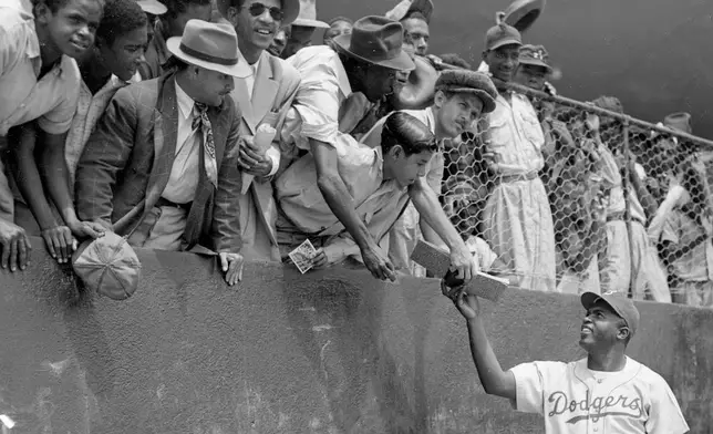 FILE - Jackie Robinson, first baseman of the Brooklyn Dodgers, returns an autograph book to a fan in the stands, during the Dodgers' spring training in Ciudad Trujillo, now Santo Domingo, in the Dominican Republic, on March 6, 1948. (AP Photo/File)