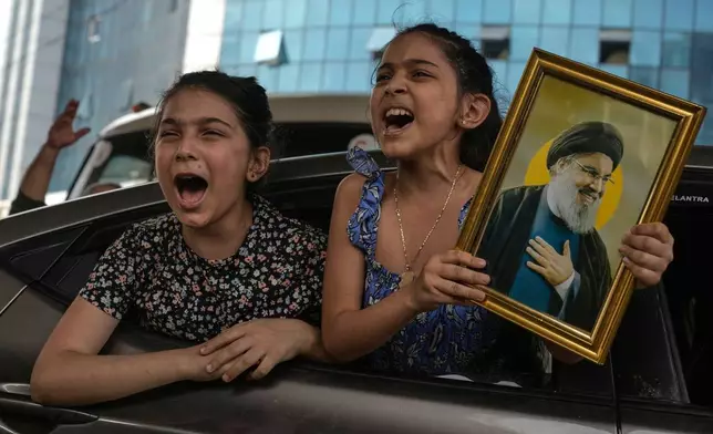 Two girls chant slogans as one holds an image of the late Hezbollah leader Hassan Nasrallah in Dahiyeh, Beirut's southern suburbs, Lebanon, Friday, April 17, 2026, following a ceasefire between Israel and Hezbollah. (AP Photo/Bilal Hussein)