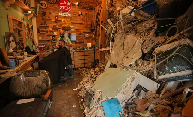 Barber Mohammad Mehdi cuts the hair of his client Ayman Al Zein inside his shop, which was damaged in an Israeli airstrike that also damaged Al Zein's shop, in Dahiyeh, Beirut's southern suburbs, Lebanon, Saturday, April 18, 2026. (AP Photo/Hassan Ammar)